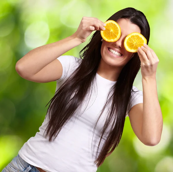 Retrato de una mujer joven sosteniendo rebanadas de naranja delante de su ey —  Fotos de Stock
