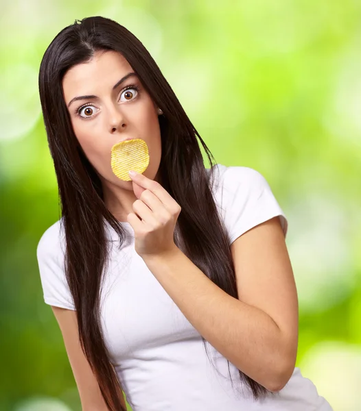 Retrato de una mujer joven sosteniendo papas fritas en su boca contra — Foto de Stock