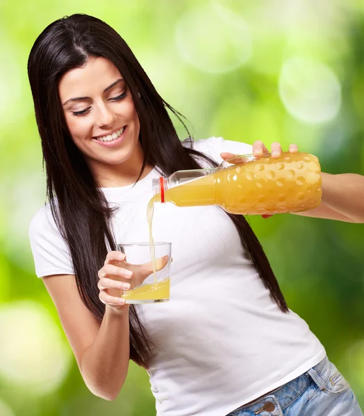 Portrait of young woman pouring orange juice on glass against a — Stock Photo, Image