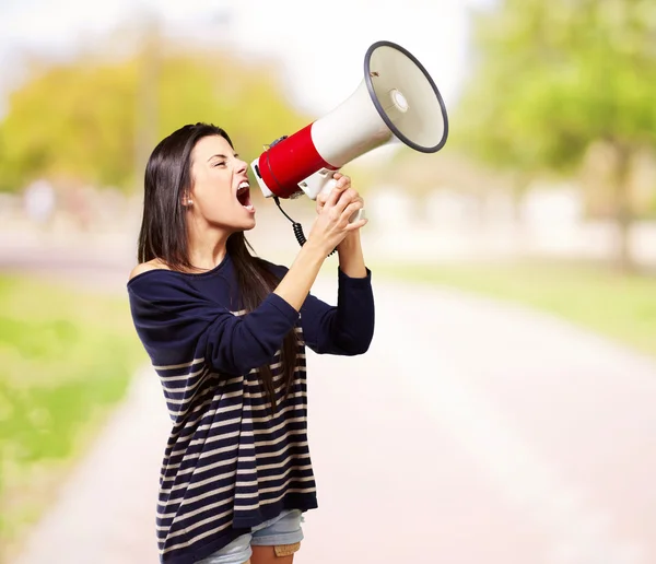 Retrato de mujer joven gritando con megáfono en el parque — Foto de Stock