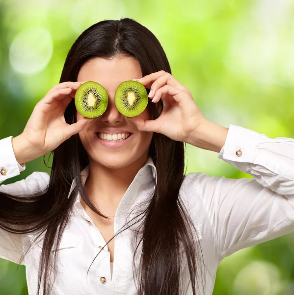 Portrait of young girl holding kiwi slices in front of her eyes — Stock Photo, Image