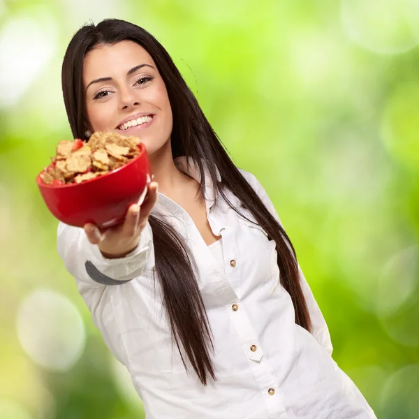 Retrato de mulher jovem oferecendo tigela de cereais contra uma natureza b — Fotografia de Stock