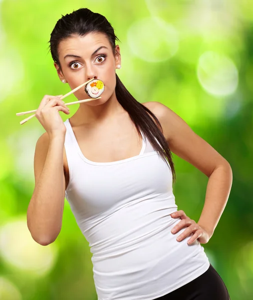 Mujer joven cubriéndose la boca con una pieza de sushi contra un natu —  Fotos de Stock
