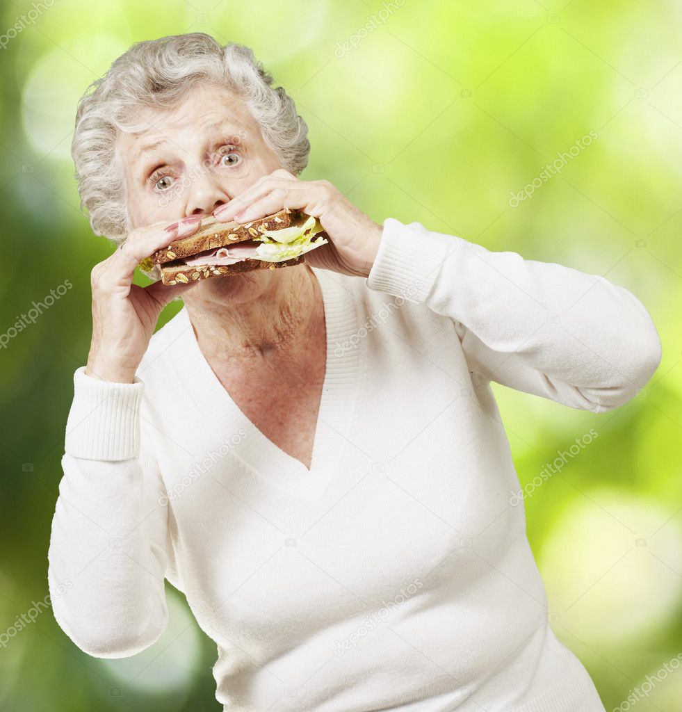 Senior woman eating a healthy sandwich against a nature backgrou