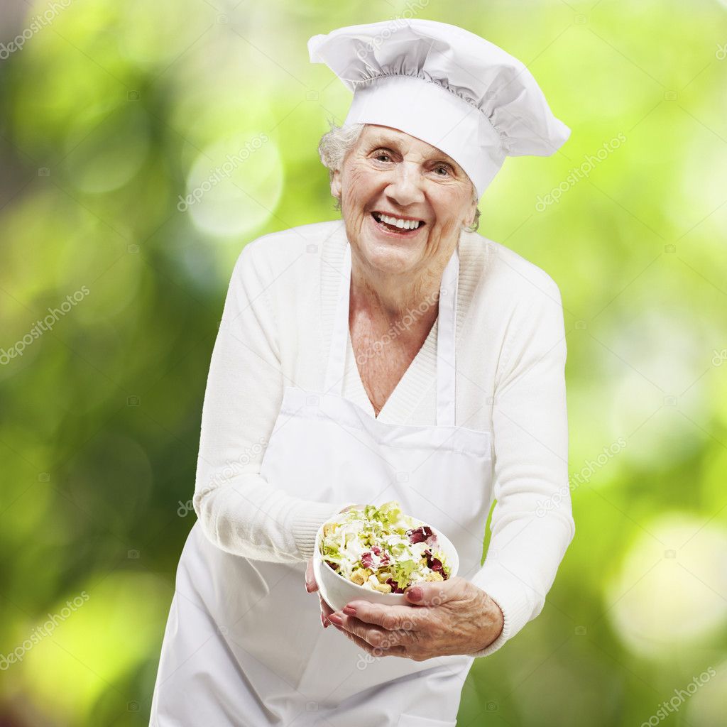 Senior woman cook holding a bowl with salad against a nature bac