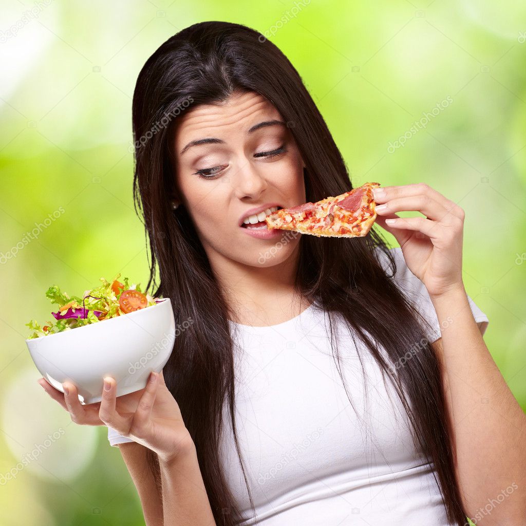 Portrait of young woman eating pizza and looking salad against a