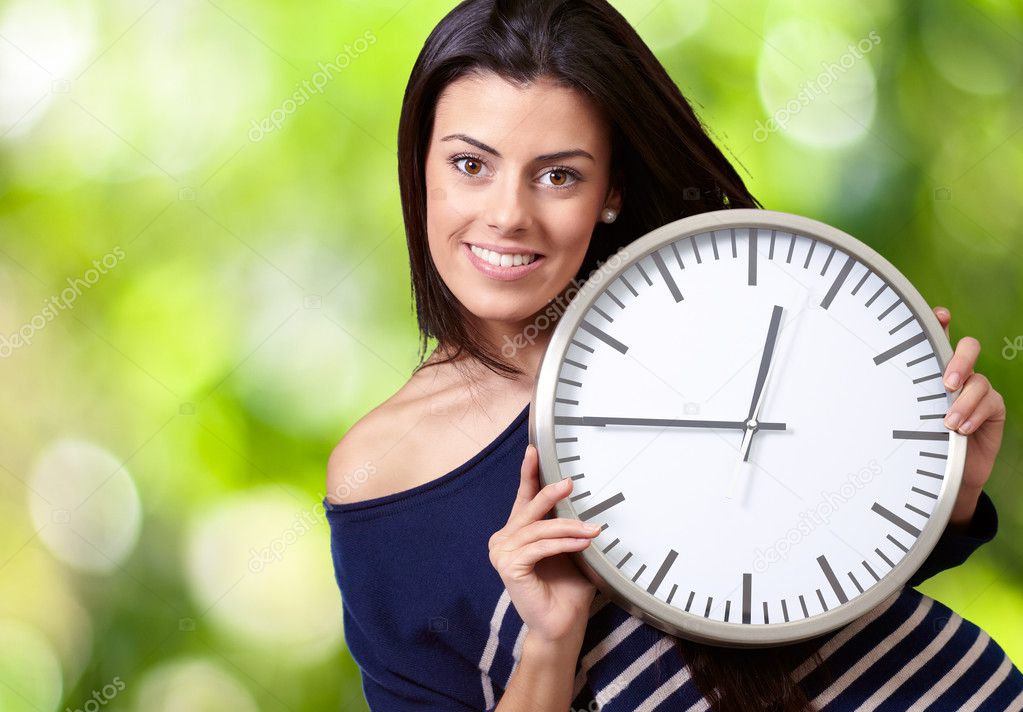 Portrait of young woman holding clock against a nature backgroun