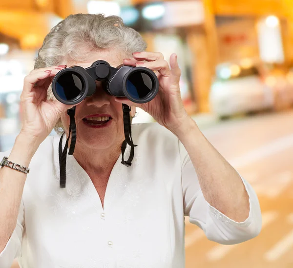Retrato de uma mulher idosa olhando através de binóculos — Fotografia de Stock