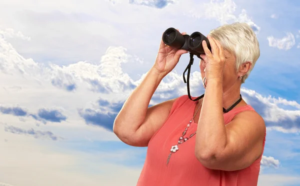 Une femme âgée regardant à travers les jumelles — Photo