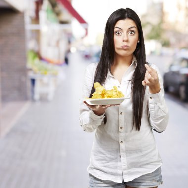 jonge vrouw eten aardappel chips tegen een straat achtergrond