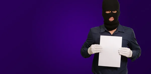 Un hombre con una máscara de ladrón mostrando un papel en blanco — Foto de Stock