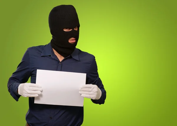 Homem usando uma máscara de ladrão mostrando um papel em branco — Fotografia de Stock