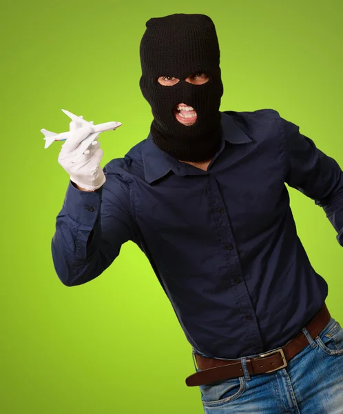 Hombre usando máscara de ladrón y sosteniendo miniatura de avión — Foto de Stock