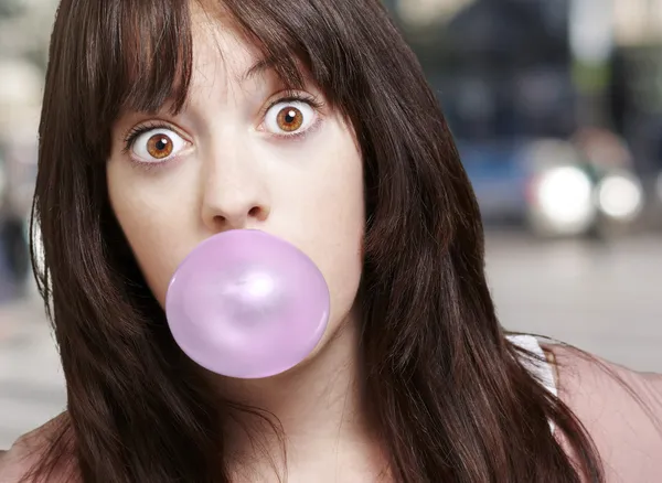 Chica joven con una burbuja rosa de goma de mascar contra una ba de la calle — Foto de Stock