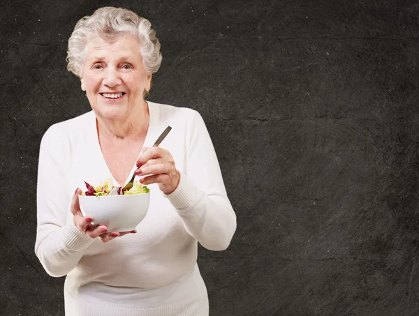 Retrato de una mujer mayor comiendo ensalada contra una pared grunge — Foto de Stock