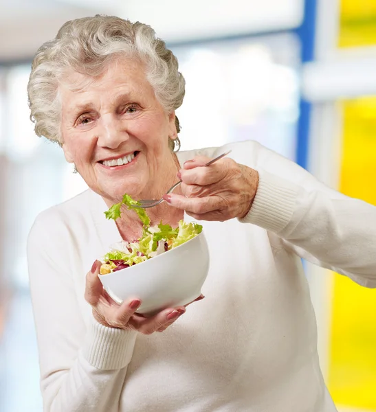 Retrato de mulher idosa comendo uma salada fresca interior — Fotografia de Stock