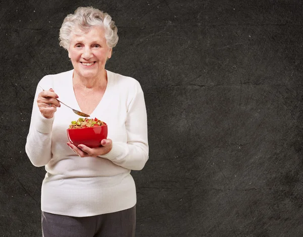 Portrait of senior woman holding a cereals bowl against a grunge — Stock Photo, Image