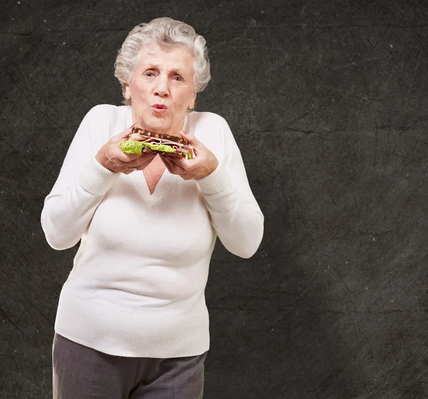 Retrato de mulher idosa segurando um delicioso sanduíche contra um — Fotografia de Stock