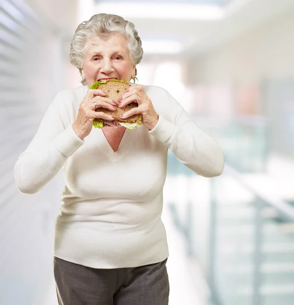 Portrait of senior woman eating vegetal sandwich at modern place — Stock Photo, Image