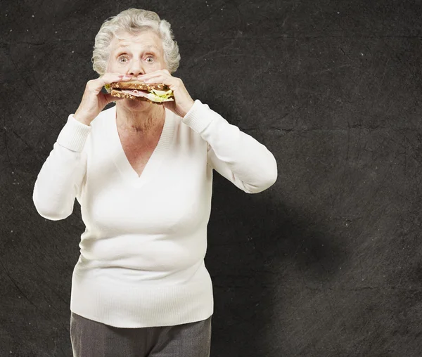 Seniorin isst vor Grunge-Hintergrund ein gesundes Sandwich — Stockfoto