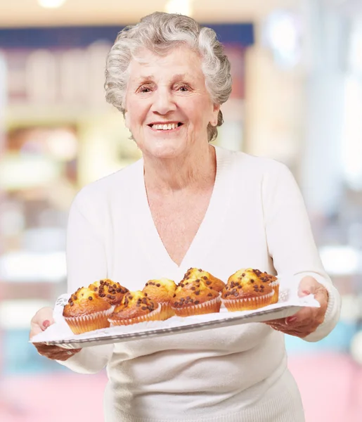 Retrato de mujer mayor mostrando una bandeja de magdalenas de chocolate en el interior — Foto de Stock