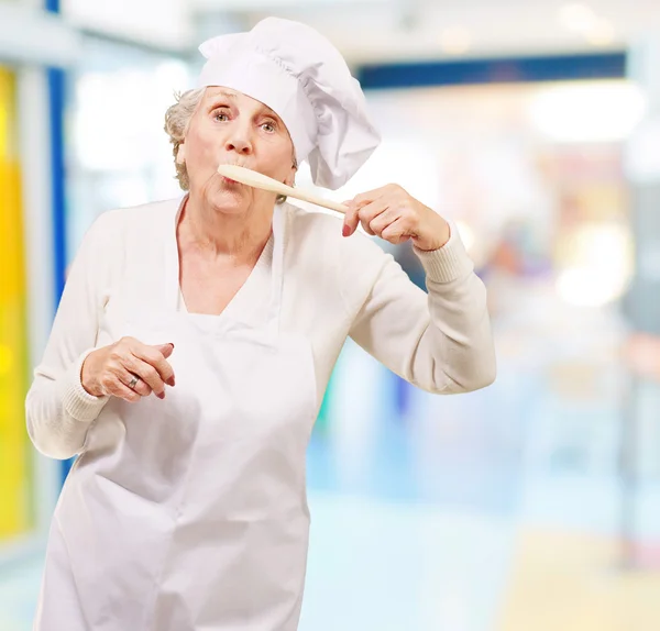 Retrato de cocinera mujer mayor con cuchara de madera en la boca interior — Foto de Stock