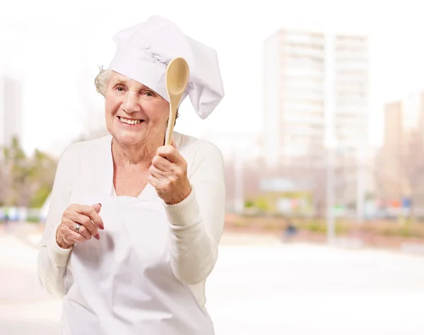 Portrait of senior cook woman holding a wooden spoon at street — Stock Photo, Image