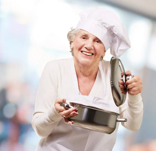 Retrato de cocinero senior mujer apertura salsa pan interior —  Fotos de Stock