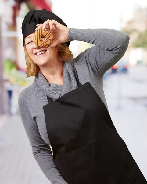Kobieta średniej wieku cook patrząc przez pączka na ulicy — Zdjęcie stockowe