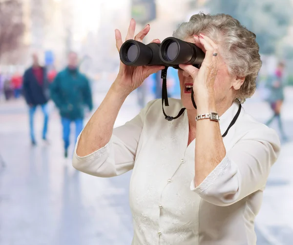 Retrato de mulher idosa olhando através de um binóculos lotados — Fotografia de Stock
