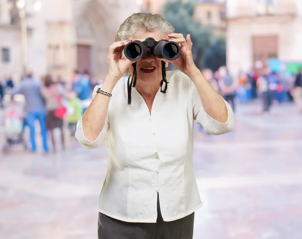 Porträt einer Seniorin, die durch ein Fernglas blickt — Stockfoto