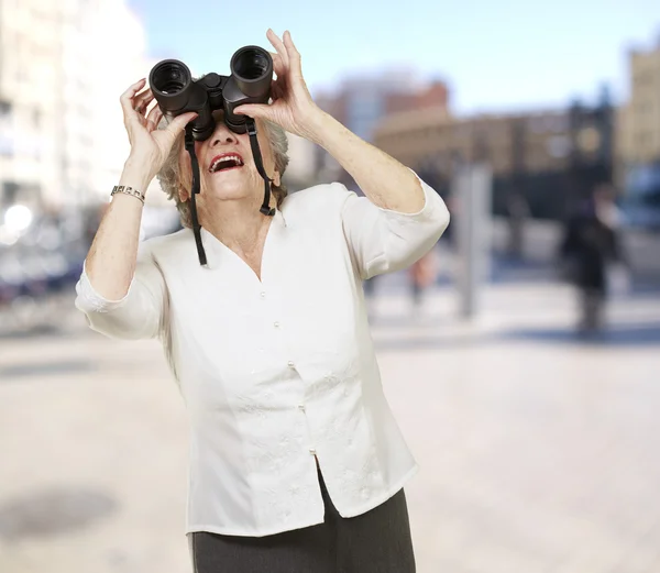 通过双筒望远镜在城市寻找高级女人肖像 — 图库照片