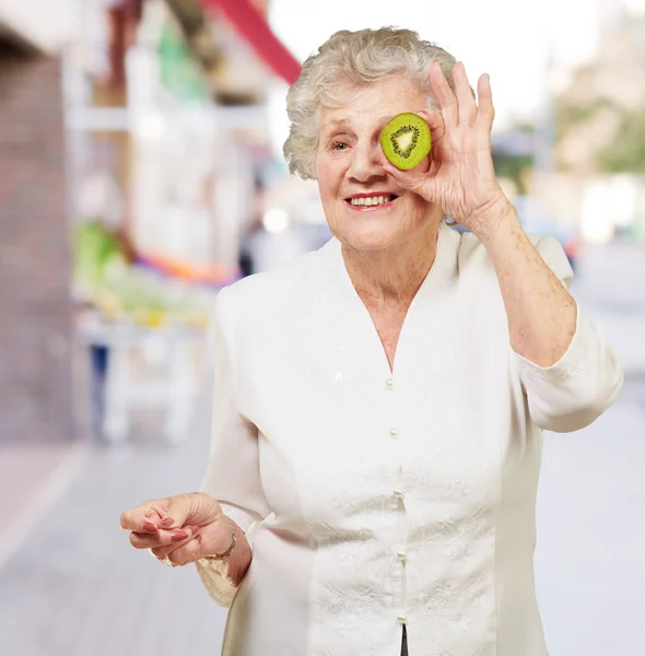 Retrato de mujer mayor sosteniendo kiwi frente a su ojo en str —  Fotos de Stock