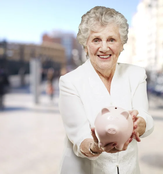 Retrato de mulher sênior mostrando um porquinho banco na cidade — Fotografia de Stock