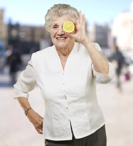 Portrait of senior woman with lemon in front of her eye against — Stock Photo, Image