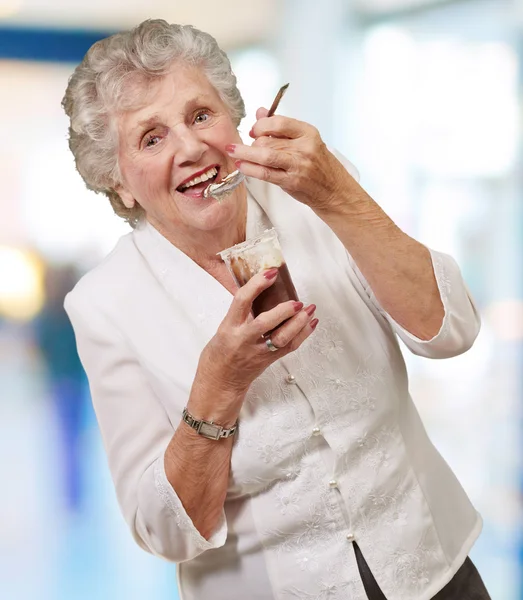 Ritratto di donna anziana che mangia cioccolato e tazza di crema al coperto — Foto Stock