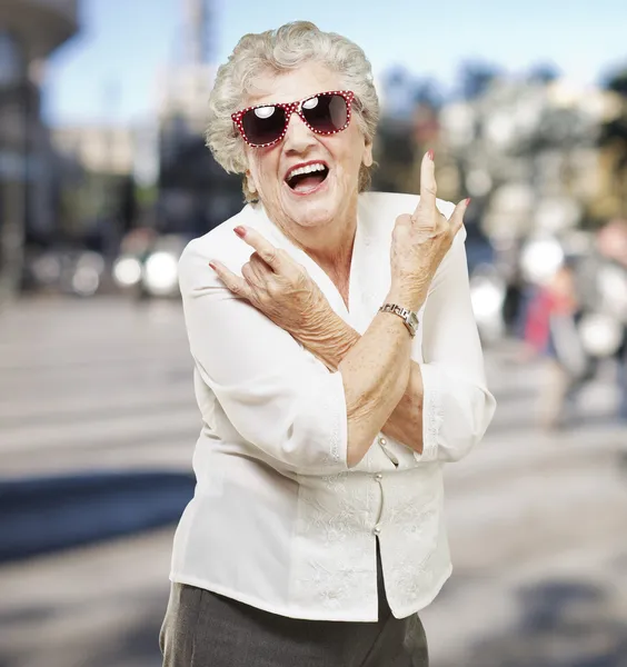 Portrait d'une femme âgée faisant un symbole rock sur fond de ville — Photo