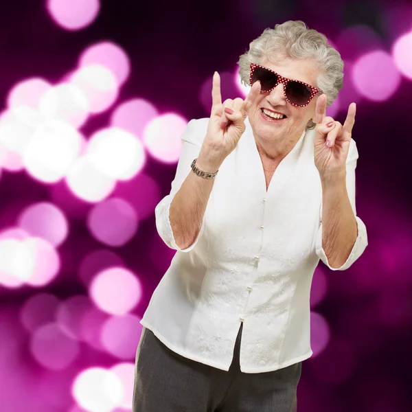 Портрет счастливой пожилой женщины, делающей рок-символ против пресса — стоковое фото