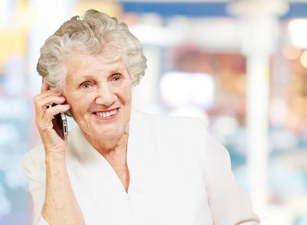 Retrato de mulher idosa falando no celular contra um ba abstrato — Fotografia de Stock
