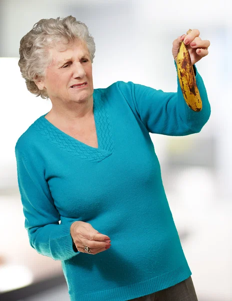 Senior femeie holding o banana putred indoor — Fotografie, imagine de stoc