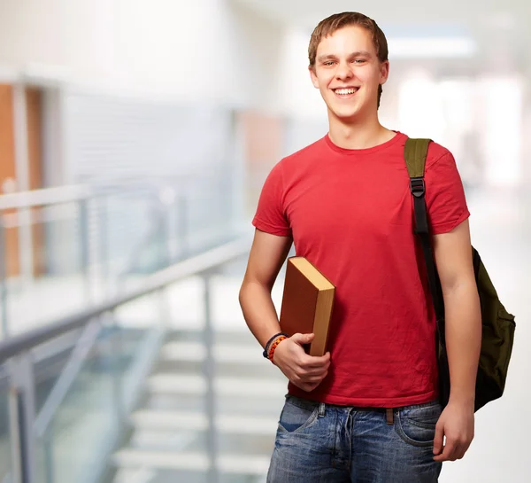 Retrato del joven estudiante sosteniendo el libro y llevando la mochila en —  Fotos de Stock