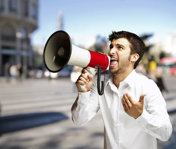 Portrait of young man shouting with megaphone at street — Stock Photo, Image