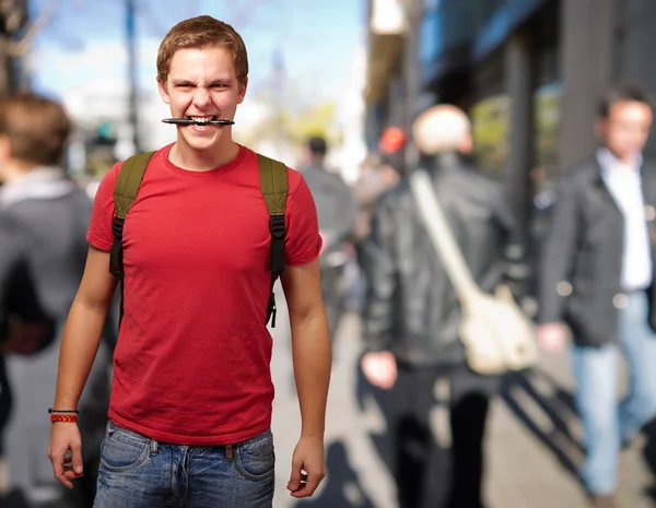 Portrait of angry young man biting pen at crowded street — Stock Photo, Image