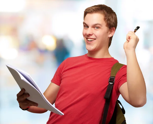 Retrato de un estudiante guapo sosteniendo un cuaderno y una pluma contra un —  Fotos de Stock