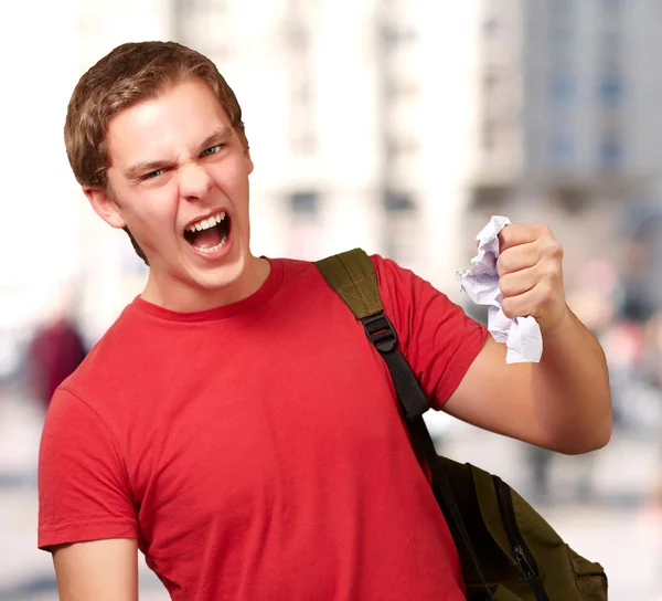 Joven estudiante enojado golpeando una hoja contra una universidad — Foto de Stock