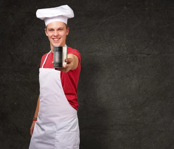Portrait of young cook man holding a metal tin can against a gru — Stock Photo, Image