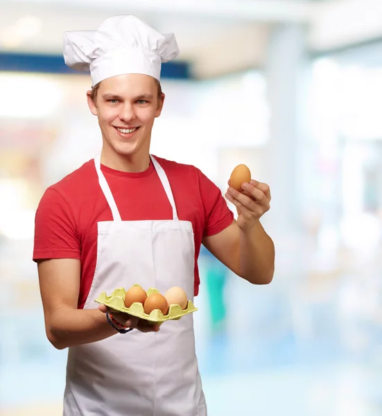 Portrait of young cook man holding egg box indoor — Stock Photo, Image