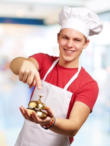 Портрет молодого кухаря, який натискає на золотий дзвін у приміщенні — стокове фото