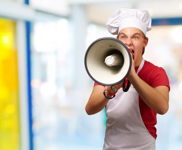 Retrato de jovem cozinheiro gritando com megafone interior — Fotografia de Stock