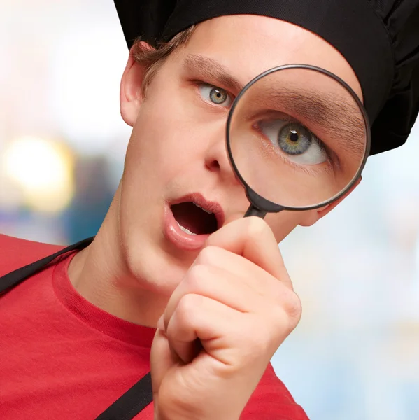 Portrait of young cook man looking through a magnifying glass in — Stock fotografie